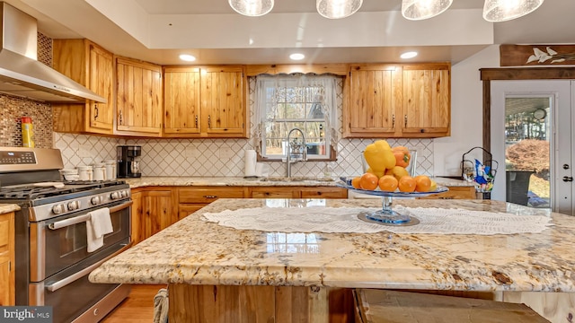 kitchen with wall chimney exhaust hood, double oven range, light stone countertops, and a sink