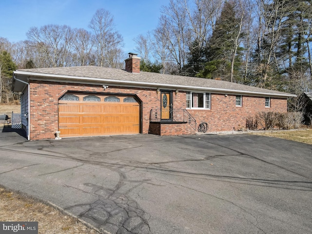 ranch-style home with driveway, an attached garage, a shingled roof, brick siding, and a chimney