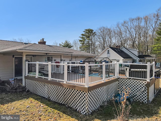 back of property featuring a shingled roof, a deck, and a chimney