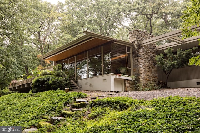 exterior space featuring stairway, a sunroom, a chimney, and stone siding