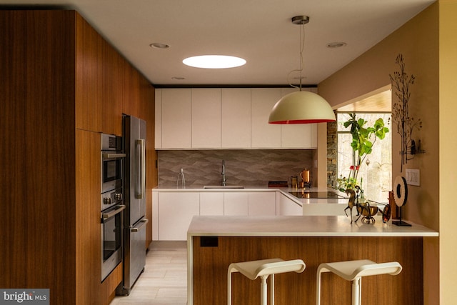 kitchen featuring a sink, freestanding refrigerator, a peninsula, decorative backsplash, and modern cabinets