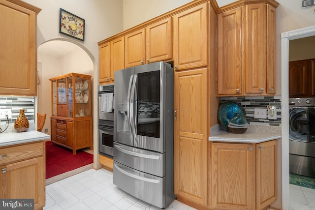 kitchen with stainless steel appliances, arched walkways, light colored carpet, decorative backsplash, and light stone counters
