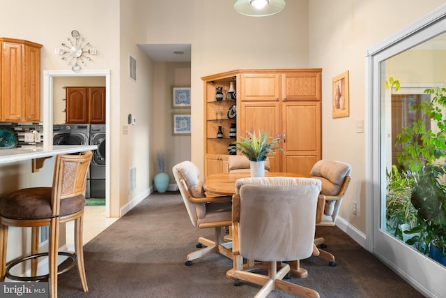 dining space featuring a towering ceiling, dark colored carpet, washer and clothes dryer, and visible vents