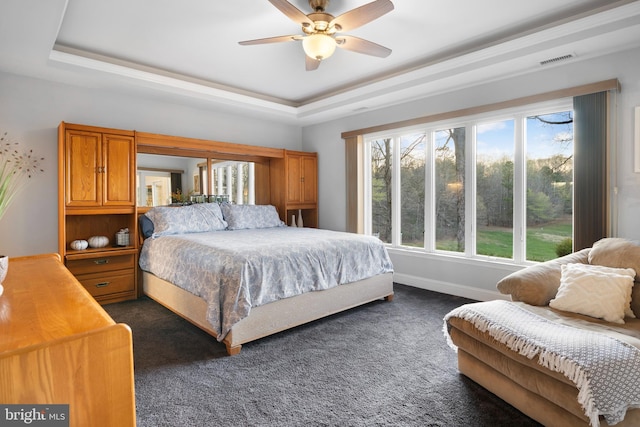 bedroom featuring a tray ceiling, dark colored carpet, visible vents, and a ceiling fan