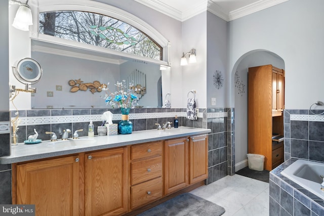 full bath with tile walls, ornamental molding, a relaxing tiled tub, and a sink
