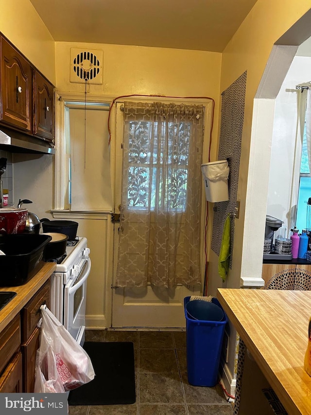 2834 Edgecombe Cir S, Baltimore, MD 21215 - kitchen with under cabinet range hood, butcher block countertops, white gas stove, dark tile patterned flooring, and dark brown cabinets
