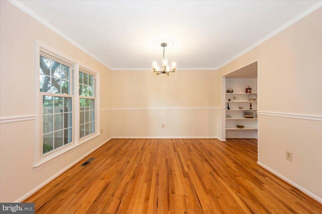 unfurnished dining area with a chandelier, wood finished floors, ornamental molding, baseboards, and built in shelves
