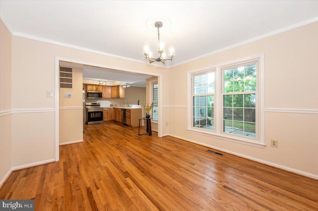 unfurnished dining area with a chandelier, ornamental molding, wood finished floors, baseboards, and a sink
