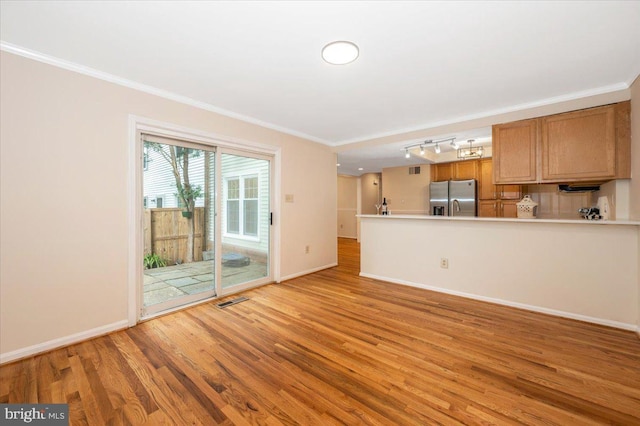 unfurnished living room with light wood-type flooring, ornamental molding, baseboards, and track lighting