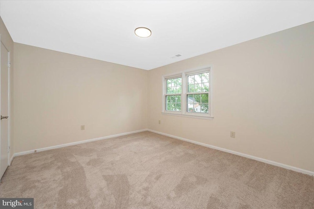 spare room featuring light colored carpet and baseboards
