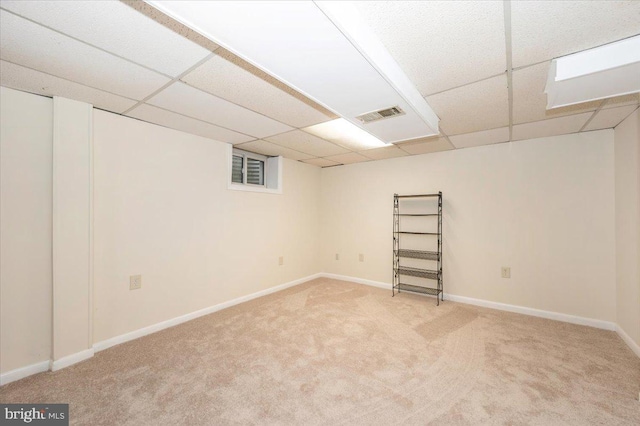 finished below grade area featuring light carpet, a drop ceiling, and baseboards