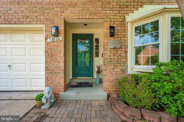 view of exterior entry with brick siding and a garage