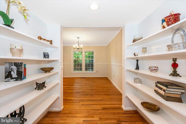 corridor with a chandelier, wood finished floors, and ornamental molding