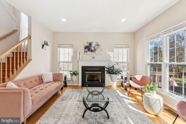 living area featuring wood finished floors, baseboards, a fireplace with flush hearth, recessed lighting, and stairs
