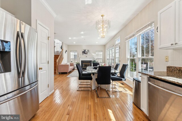 dining room with a notable chandelier, a glass covered fireplace, crown molding, and light wood-type flooring