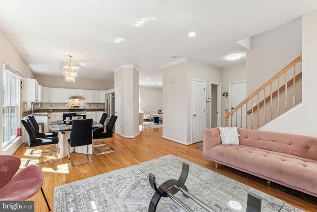living area featuring baseboards, light wood finished floors, ornamental molding, stairs, and a notable chandelier