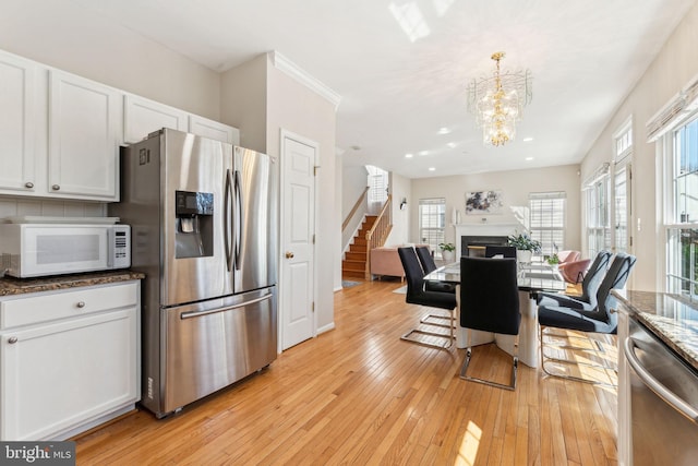 kitchen with light wood finished floors, dark stone countertops, appliances with stainless steel finishes, and white cabinetry