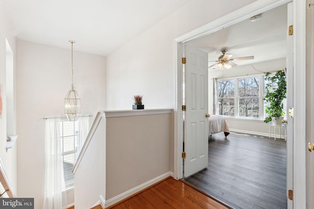 hall featuring an upstairs landing, a notable chandelier, a healthy amount of sunlight, and wood finished floors