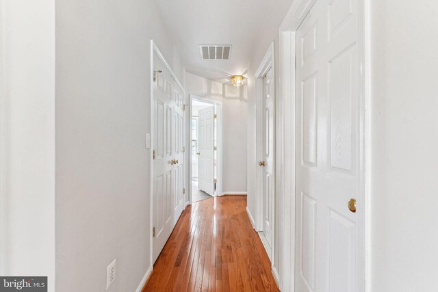 hall with hardwood / wood-style flooring, baseboards, and visible vents