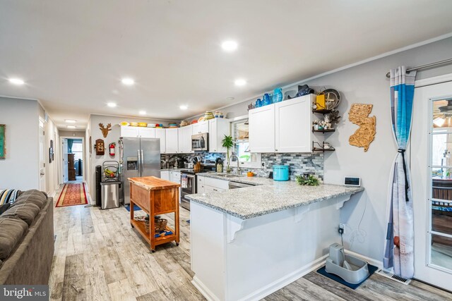 kitchen with light wood finished floors, appliances with stainless steel finishes, a breakfast bar, and a peninsula