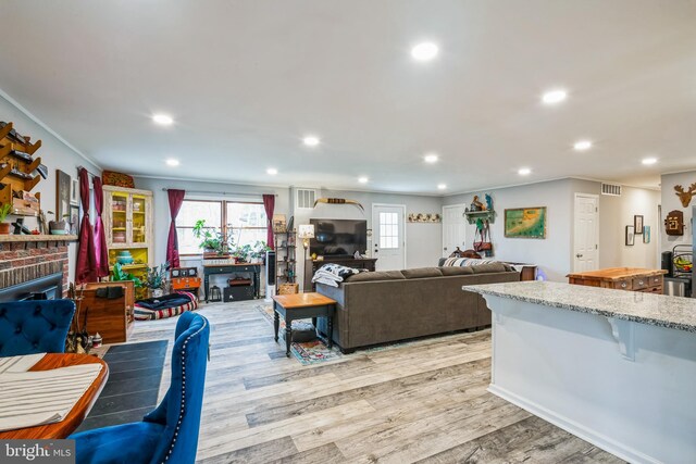 living room featuring visible vents, light wood-style flooring, a fireplace, recessed lighting, and ornamental molding