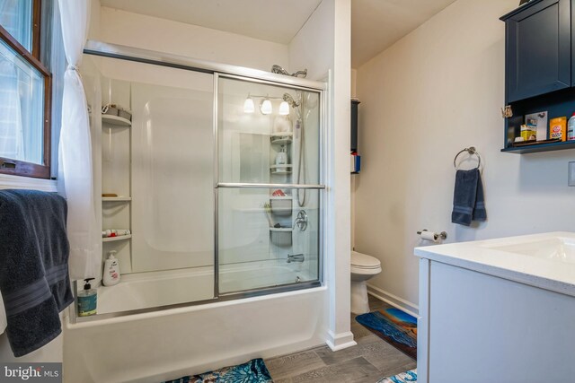 bathroom with combined bath / shower with glass door, toilet, vanity, and wood finished floors