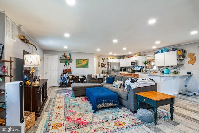 living area featuring recessed lighting, light wood-style floors, baseboards, and ornamental molding