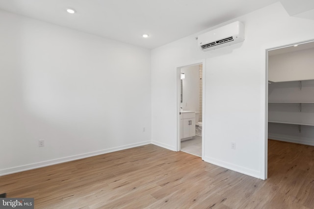 unfurnished bedroom featuring recessed lighting, light wood-style floors, an AC wall unit, and a spacious closet