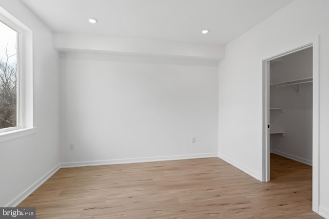 unfurnished bedroom with a spacious closet, recessed lighting, light wood-style floors, and baseboards