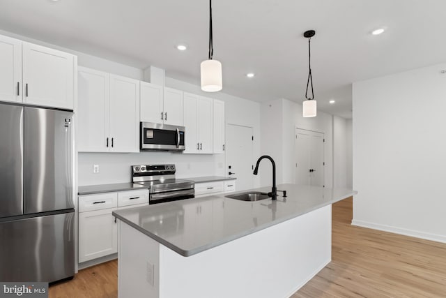 kitchen with a center island with sink, light wood-type flooring, appliances with stainless steel finishes, white cabinets, and a sink