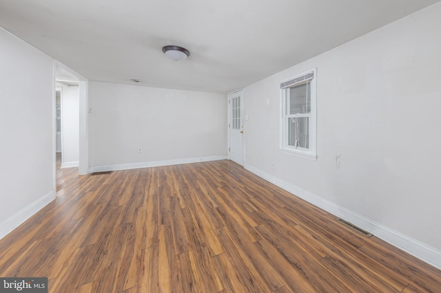 empty room with wood finished floors, visible vents, and baseboards