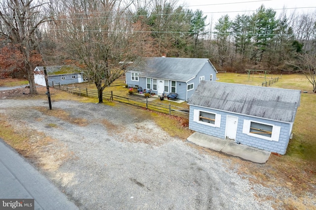 view of front facade featuring a shingled roof, gravel driveway, a front yard, and fence