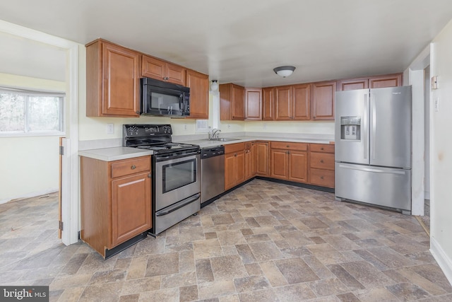 kitchen featuring light countertops, brown cabinets, stone finish floor, stainless steel appliances, and a sink