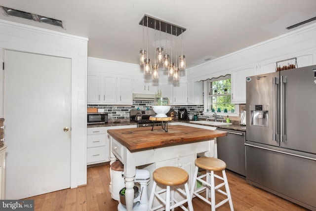 kitchen with appliances with stainless steel finishes, tasteful backsplash, white cabinetry, a sink, and butcher block countertops
