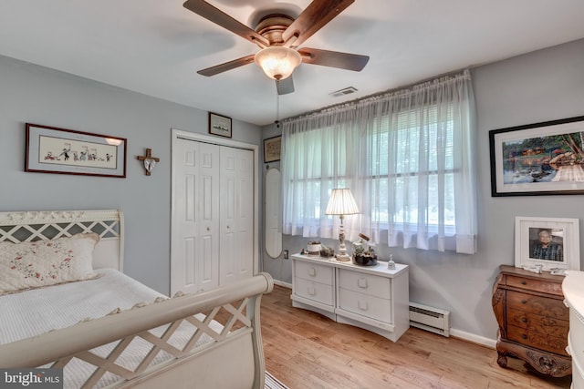 bedroom featuring visible vents, light wood-type flooring, baseboards, a closet, and a baseboard heating unit