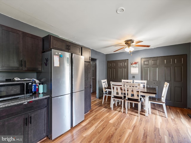kitchen with stainless steel appliances, ceiling fan, light wood-type flooring, dark brown cabinetry, and stone countertops
