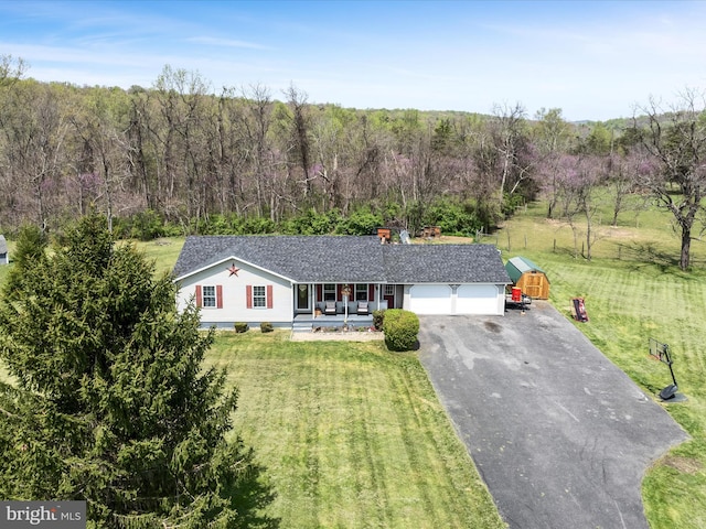 single story home featuring aphalt driveway, covered porch, a front lawn, a forest view, and a garage