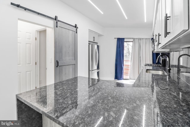 kitchen featuring a sink, a barn door, dark stone countertops, and freestanding refrigerator