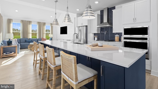kitchen featuring stainless steel appliances, decorative backsplash, light wood-style floors, wall chimney range hood, and open floor plan
