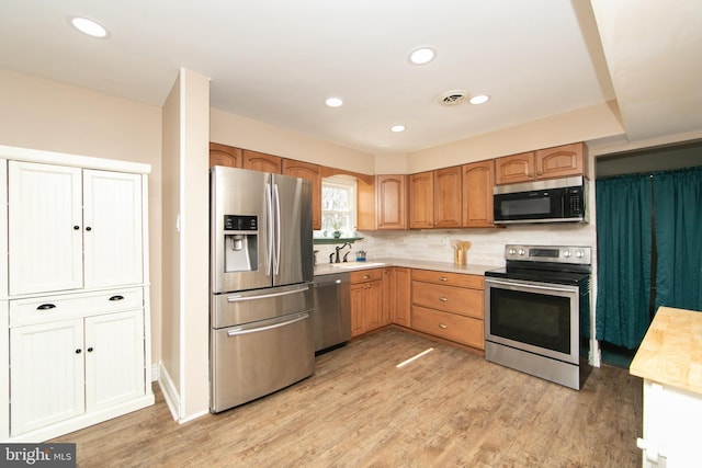 kitchen featuring light wood finished floors, light countertops, tasteful backsplash, and stainless steel appliances