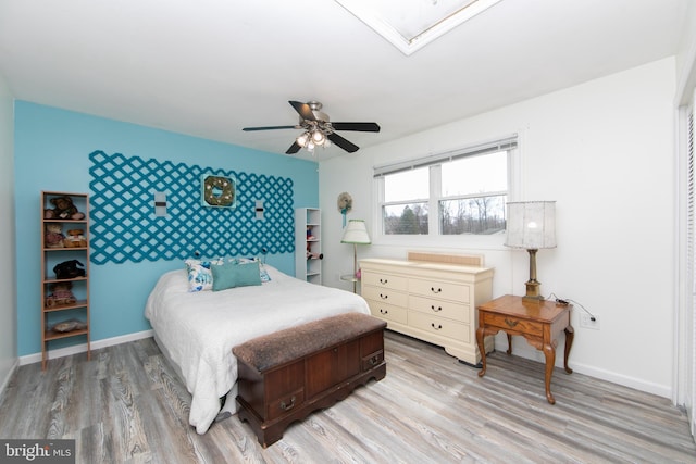 bedroom with a ceiling fan, baseboards, an accent wall, and light wood-type flooring
