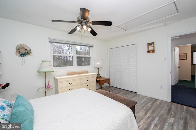 bedroom featuring a closet, attic access, wood finished floors, baseboards, and ceiling fan