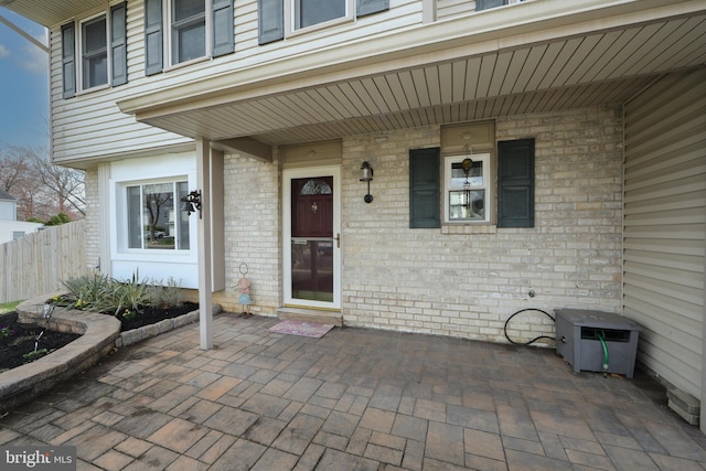 entrance to property featuring a patio, brick siding, and fence
