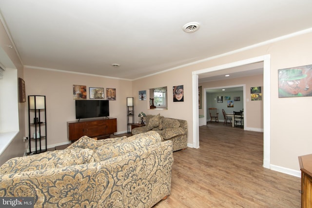 living room featuring ornamental molding, baseboards, light wood finished floors, and visible vents