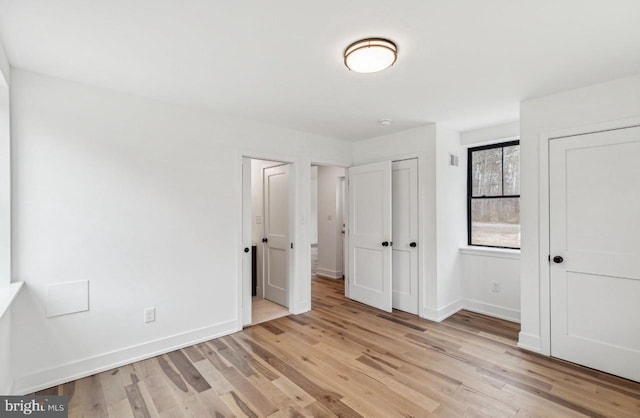 unfurnished bedroom featuring light wood-style floors, baseboards, and two closets