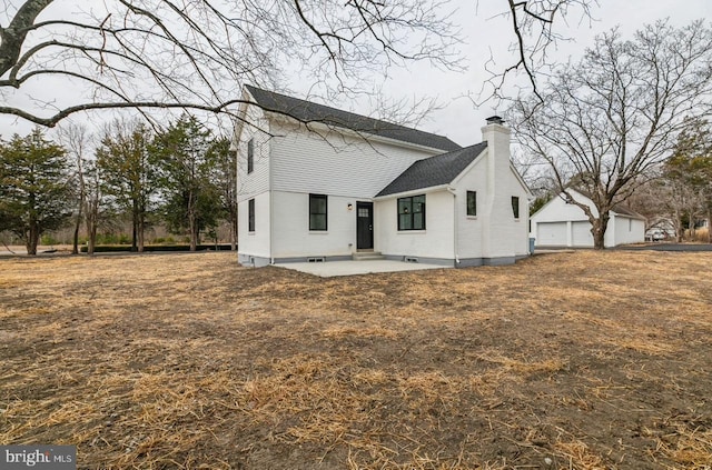 back of property featuring a shingled roof, a chimney, a garage, an outdoor structure, and a patio