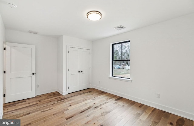 unfurnished bedroom featuring a closet, visible vents, baseboards, and light wood-style floors