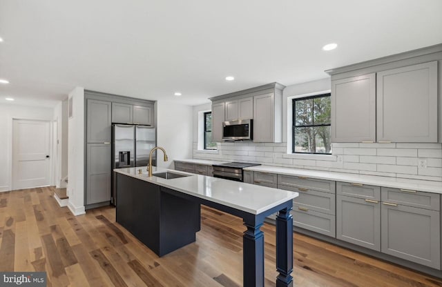 kitchen featuring backsplash, gray cabinetry, stainless steel appliances, and a sink