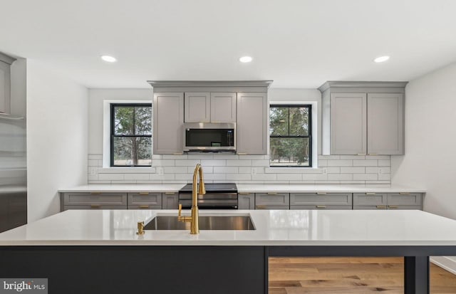 kitchen with stainless steel microwave, decorative backsplash, gray cabinets, and light countertops