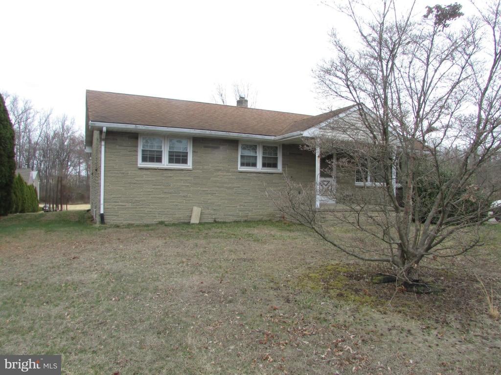 single story home featuring stone siding, a chimney, and a front lawn